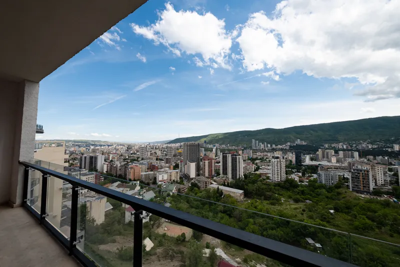 View from a balcony over central Tbilisi, with apartment blocks, trees and the hills behind the city