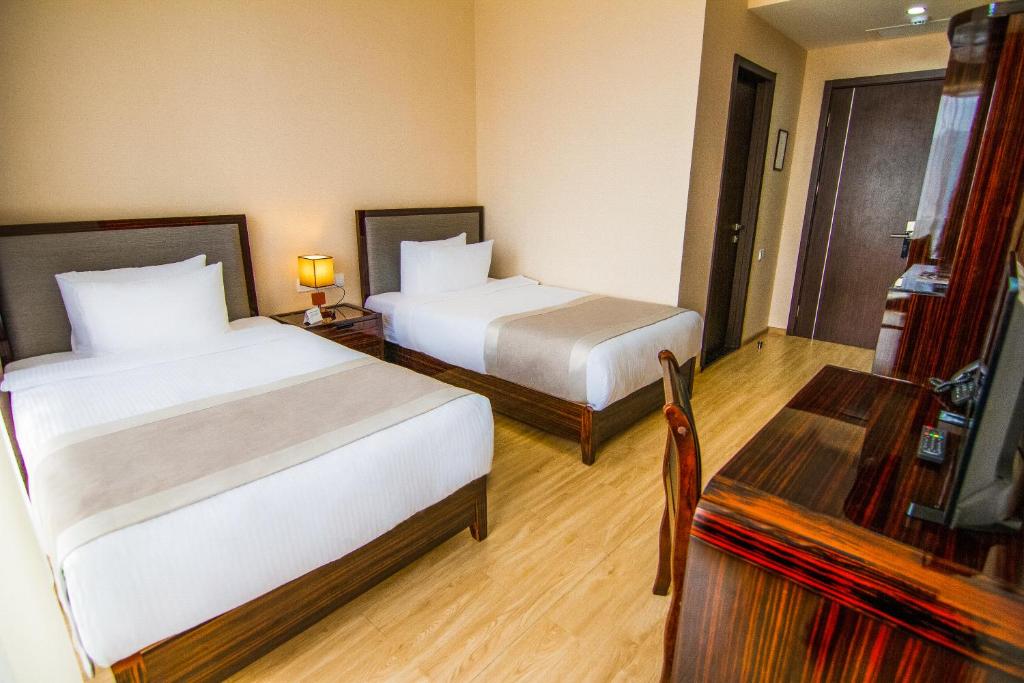 A twin hotel room with two made-up single beds, wooden floor and a desk, used for shared-room camp accommodation